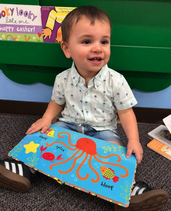 Toddler reading an ocean-themed board book at Creative Kids Academy