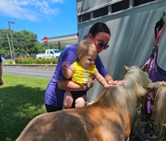 Teacher helping a baby pet a pony at a CKA family event