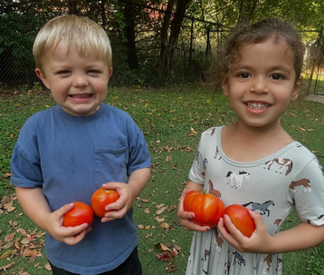 Two children proudly holding fresh tomatoes at Creative Kids Academy