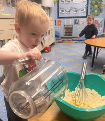 Toddler helping whisk ingredients during a cooking activity at Creative Kids Academy