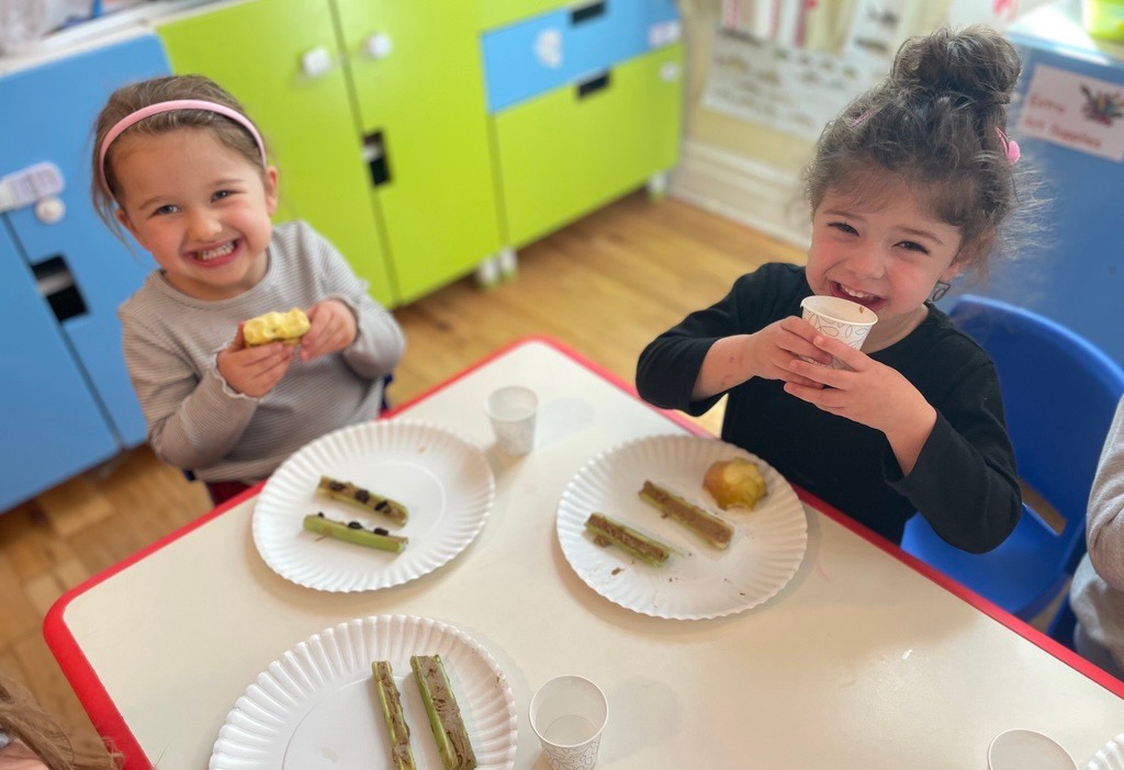 Two children smiling and enjoying snack time together at Creative Kids Academy
