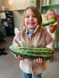 Child proudly holding a large zucchini harvested from the garden at Creative Kids Academy