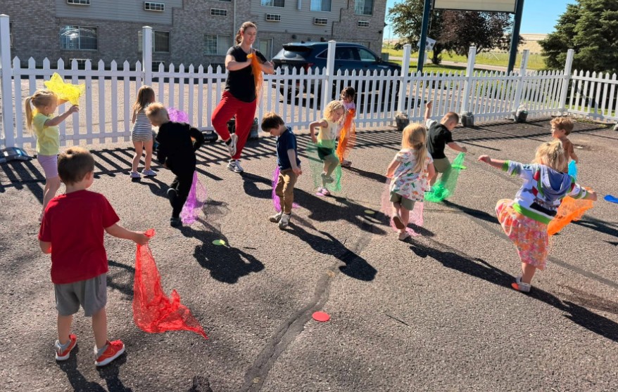 Preschoolers playing with colorful scarves outdoors at Creative Kids Academy
