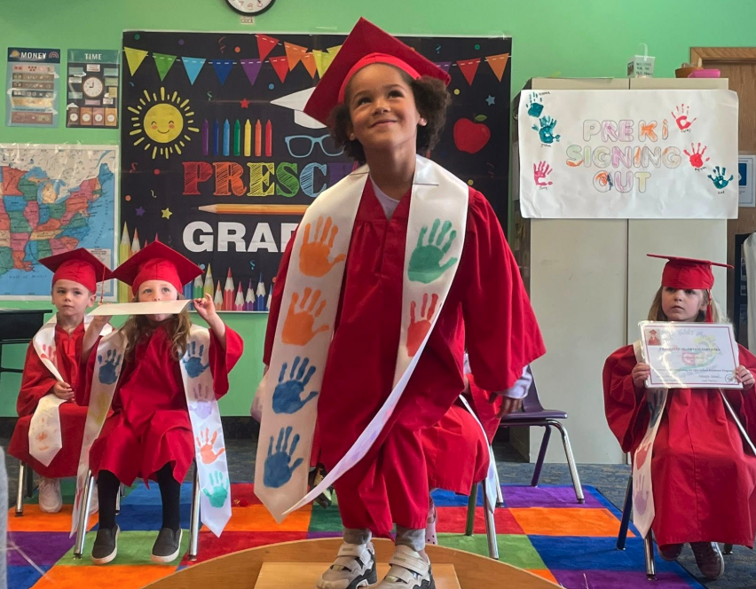 Preschoolers celebrating their preschool graduation in caps and gowns at Creative Kids Academy