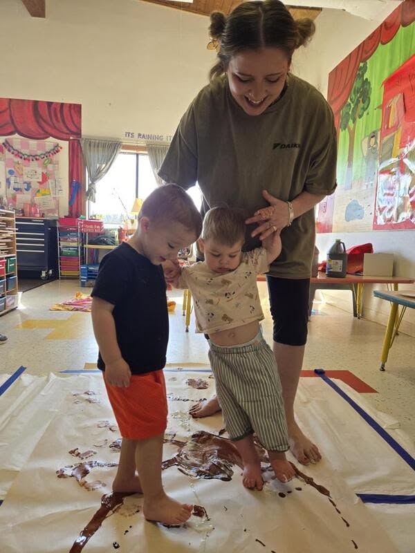 Toddlers exploring sensory footprint painting with their teacher