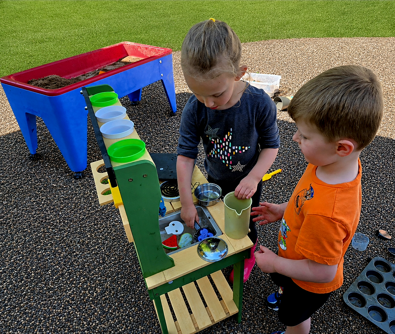 Two preschoolers exploring a mud kitchen and sensory play station outdoors at Creative Kids Academy Zimmerman