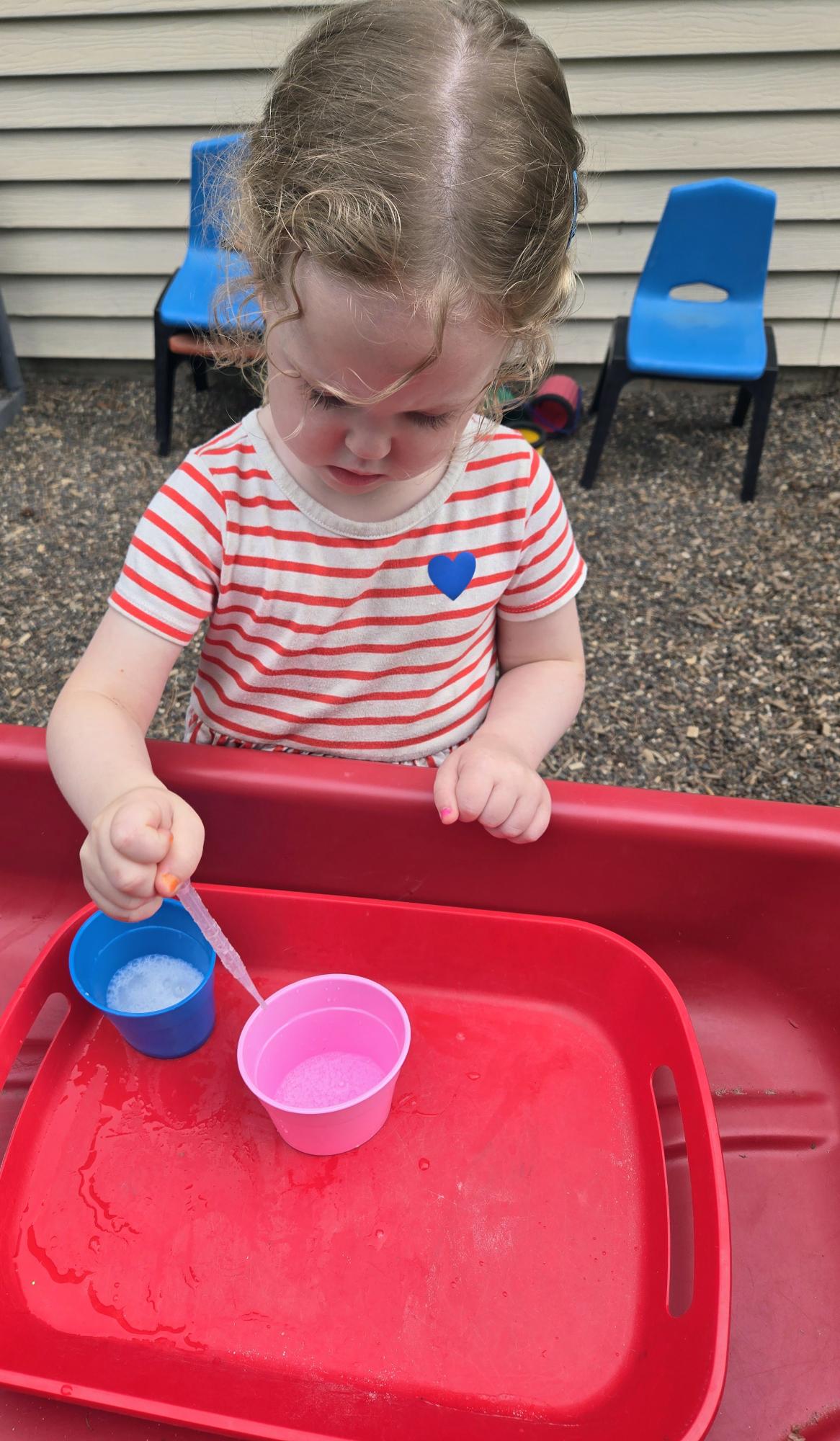A toddler exploring color mixing with droppers during an outdoor sensory science activity at Creative Kids Academy Zimmerman