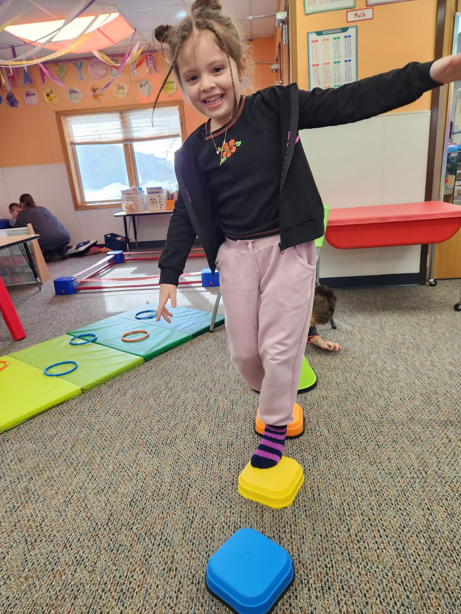 A school-age girl balancing across stepping stones during an indoor obstacle course at Creative Kids Academy Elk River on 10