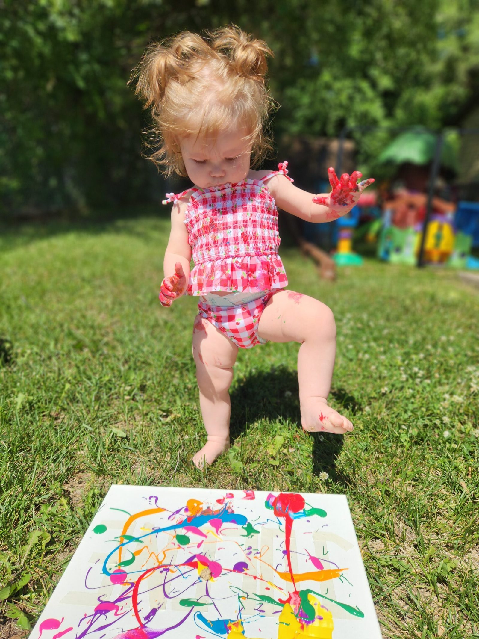 A toddler exploring paint splatter art outdoors at Creative Kids Academy Elk River on 10