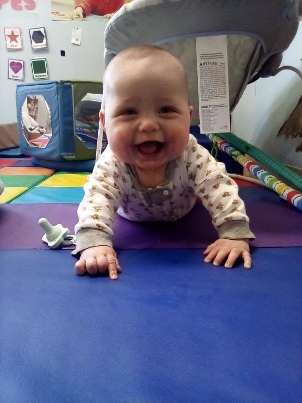 An infant crawling and smiling on a play mat at Creative Kids Academy Maplewood