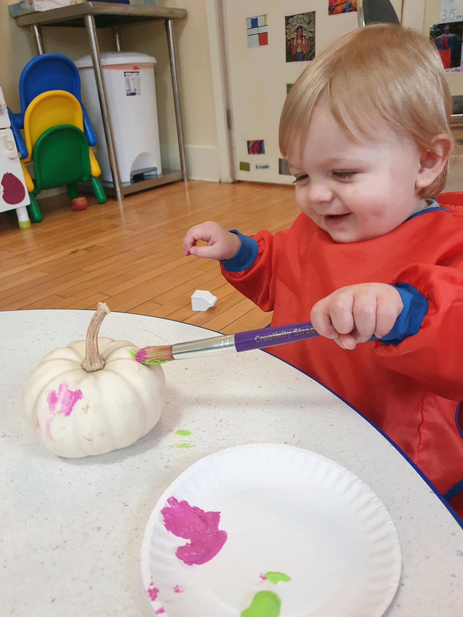 A toddler painting a pumpkin during an art activity at Creative Kids Academy Orono