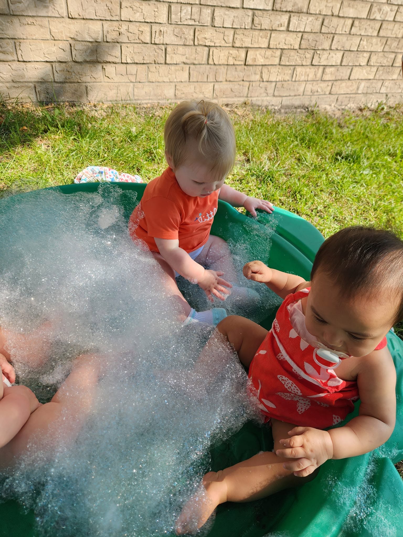 Infants playing together in a bubble-filled pool on a sunny day at Creative Kids Academy Elk River