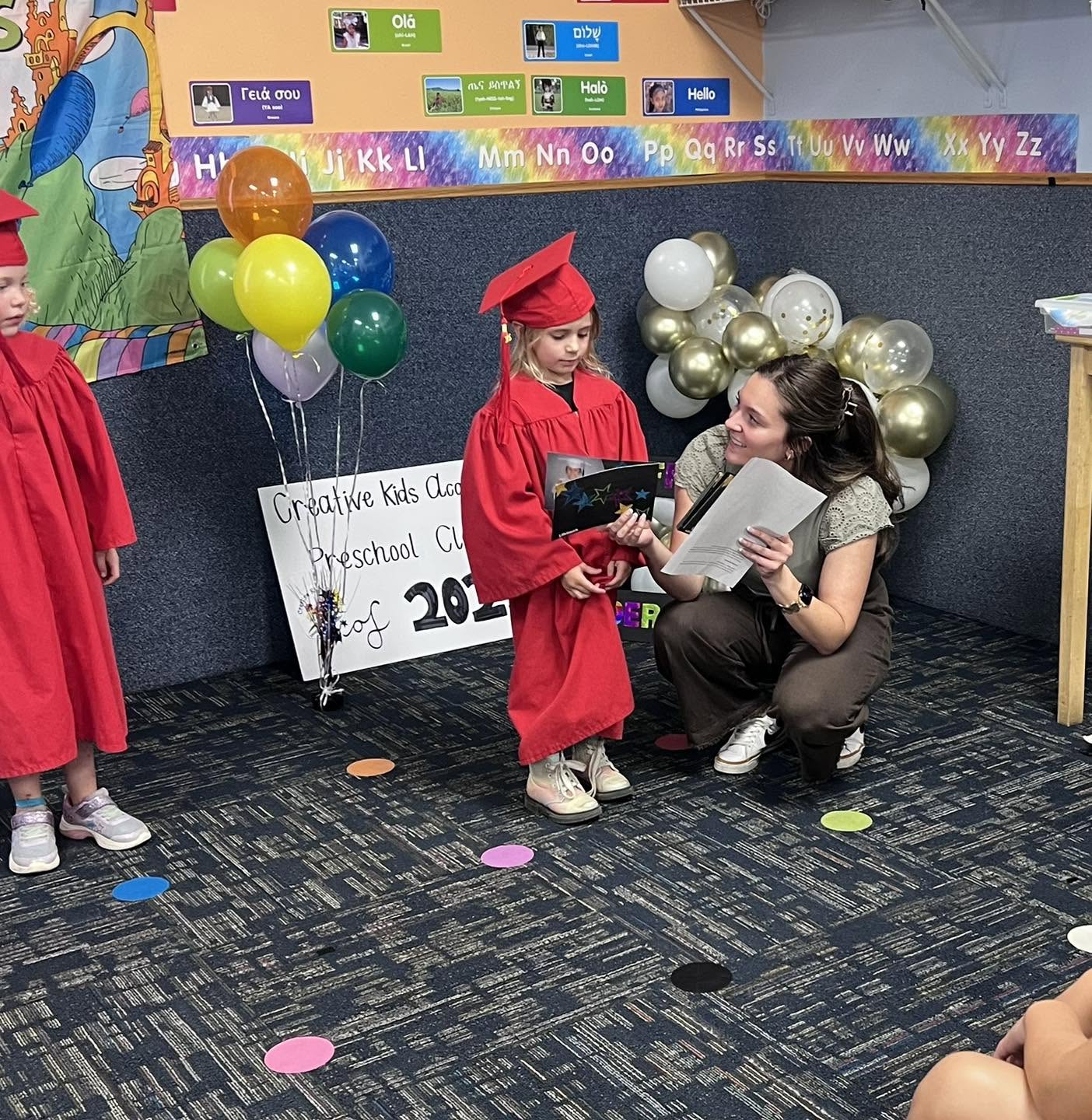 A preschool graduate receiving her diploma from a teacher at Creative Kids Academy Zimmerman