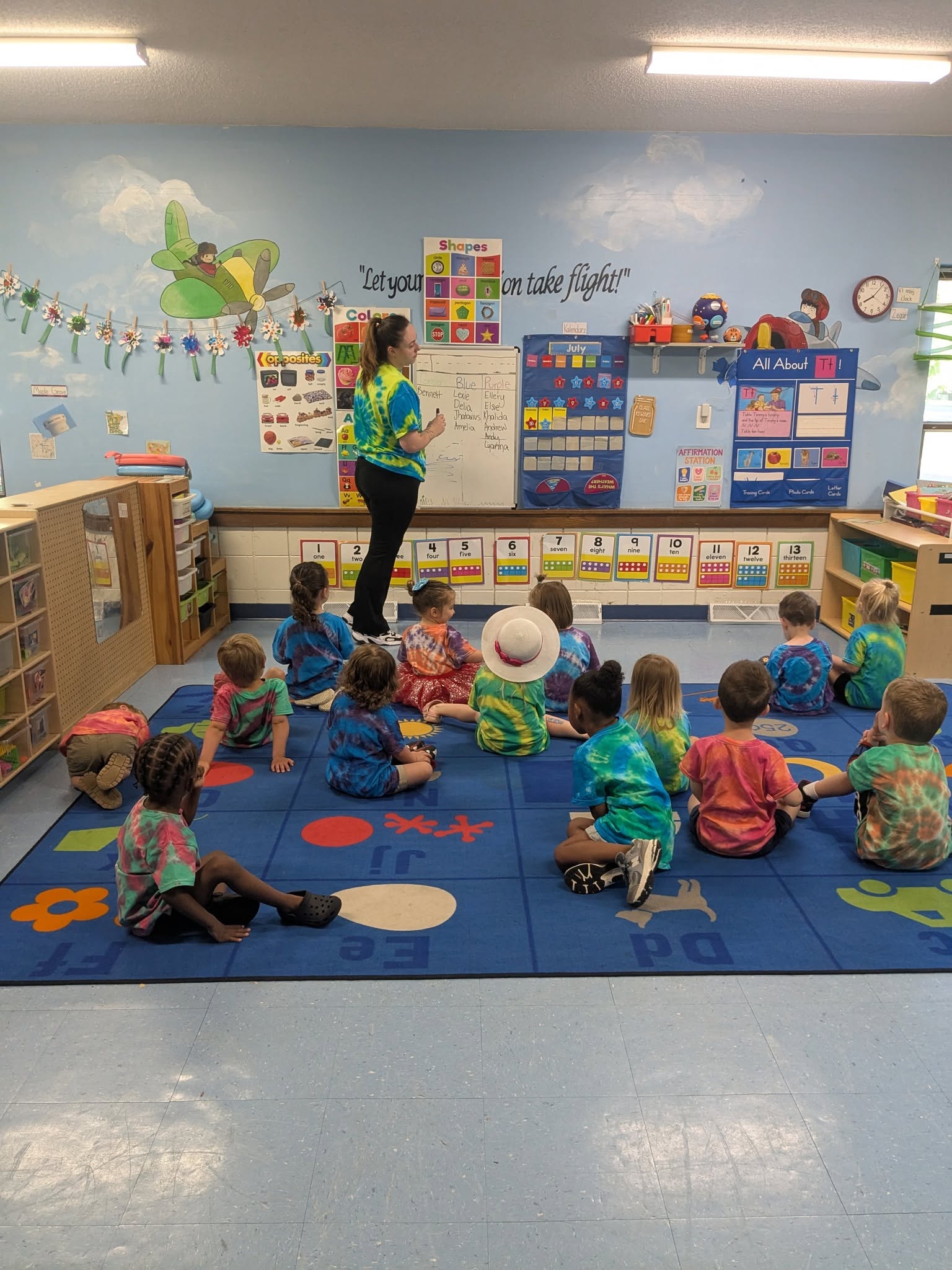 A teacher leading a tie-dye circle time activity with her class at Creative Kids Academy Maple Grove