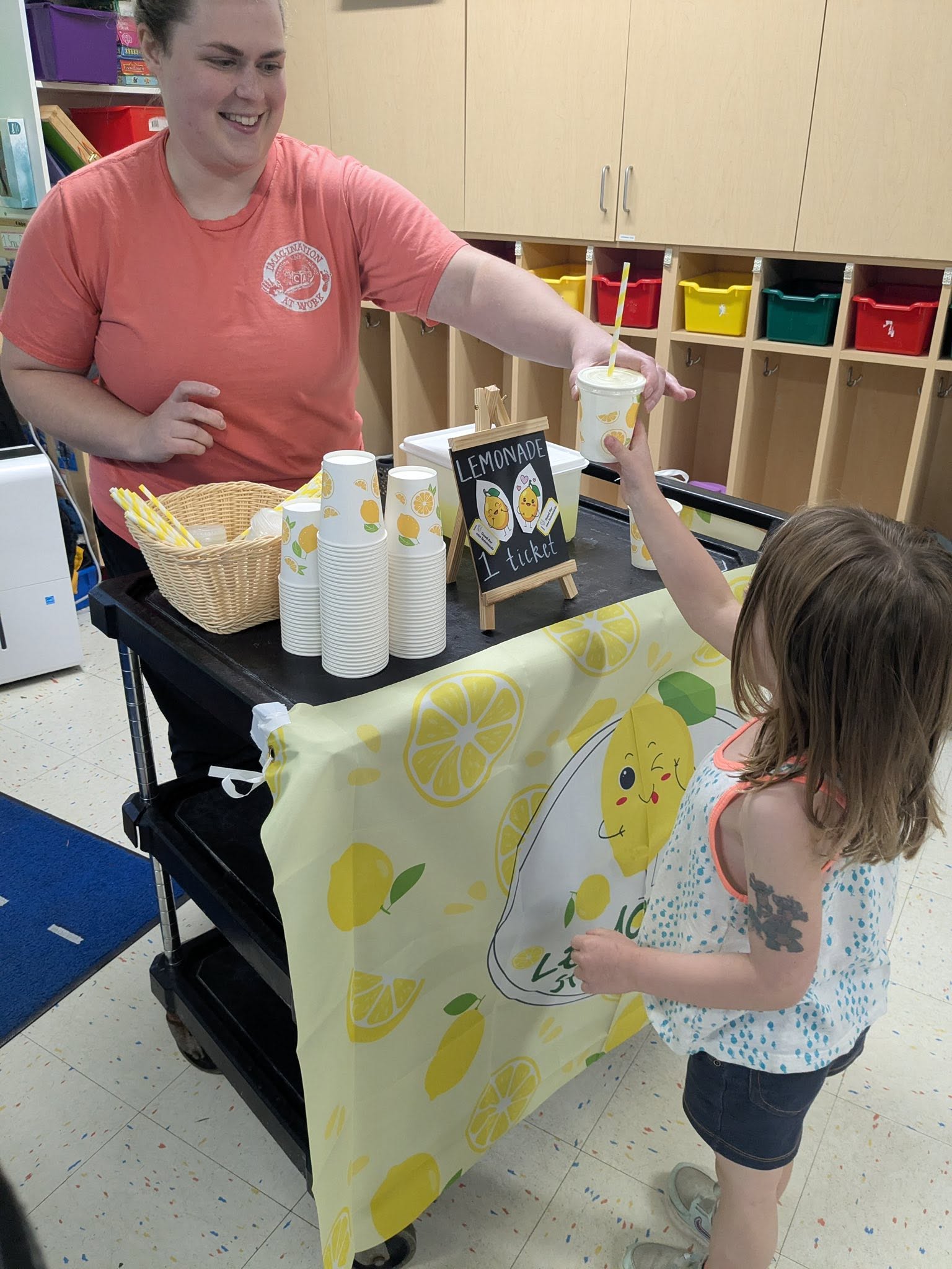 A teacher serving a child at a classroom lemonade stand at Creative Kids Academy Maple Grove