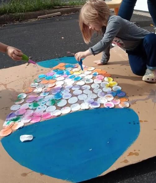A preschooler painting a large fish mural outdoors at Creative Kids Academy Maplewood