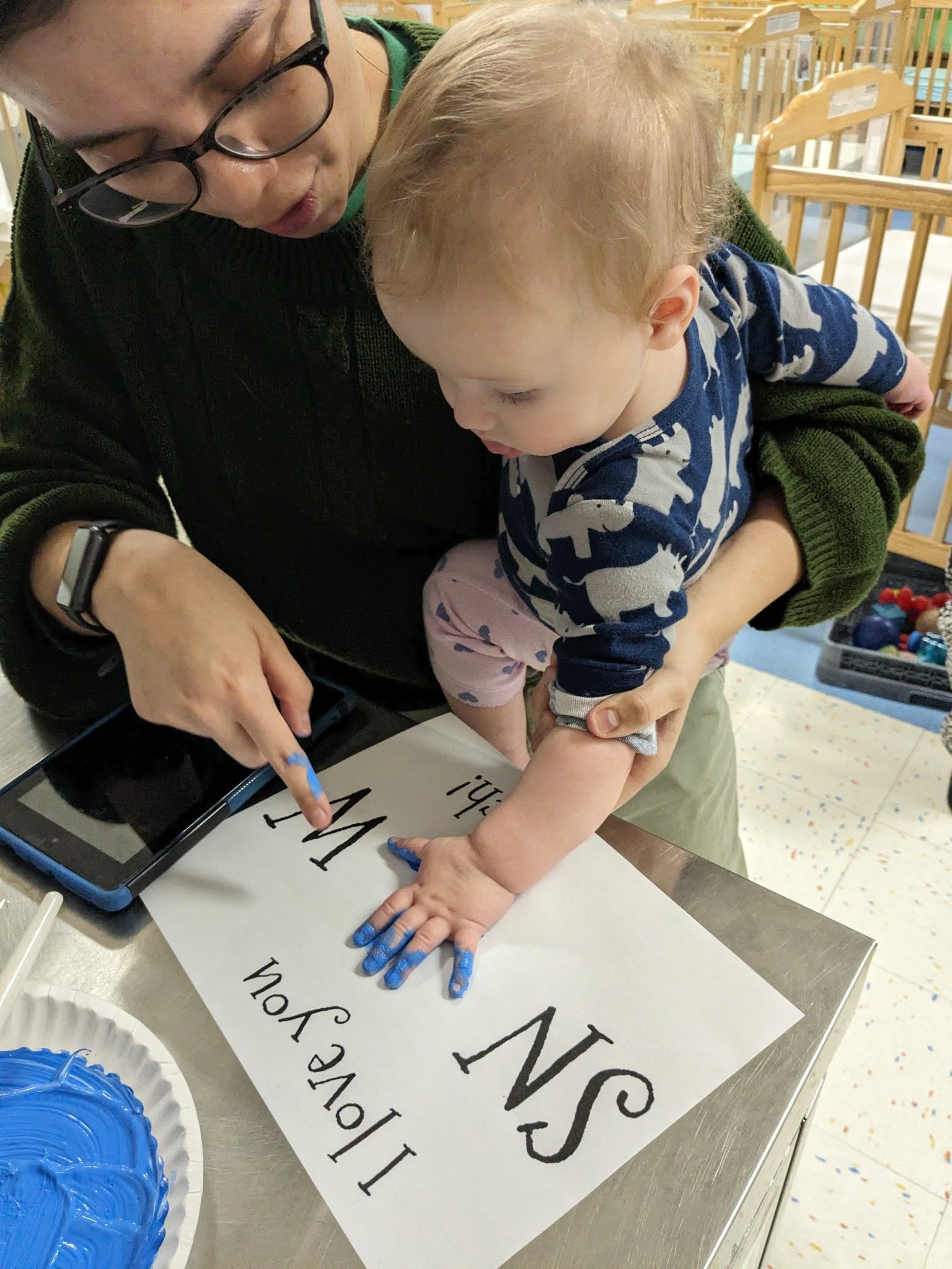 A teacher helping a toddler make a handprint painting at Creative Kids Academy Maple Grove