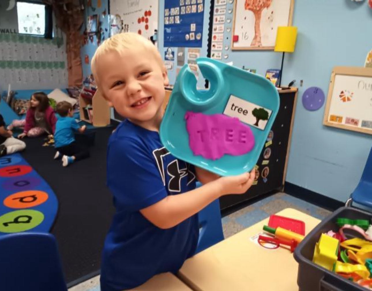 A preschooler proudly showing off a playdough letter activity at Creative Kids Academy Centerville