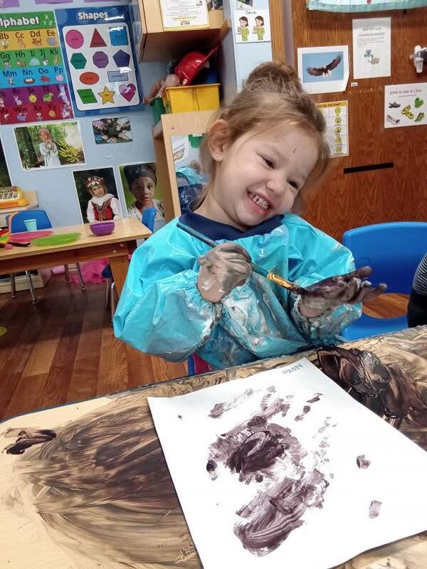 A preschooler smiling while painting at Creative Kids Academy Maplewood