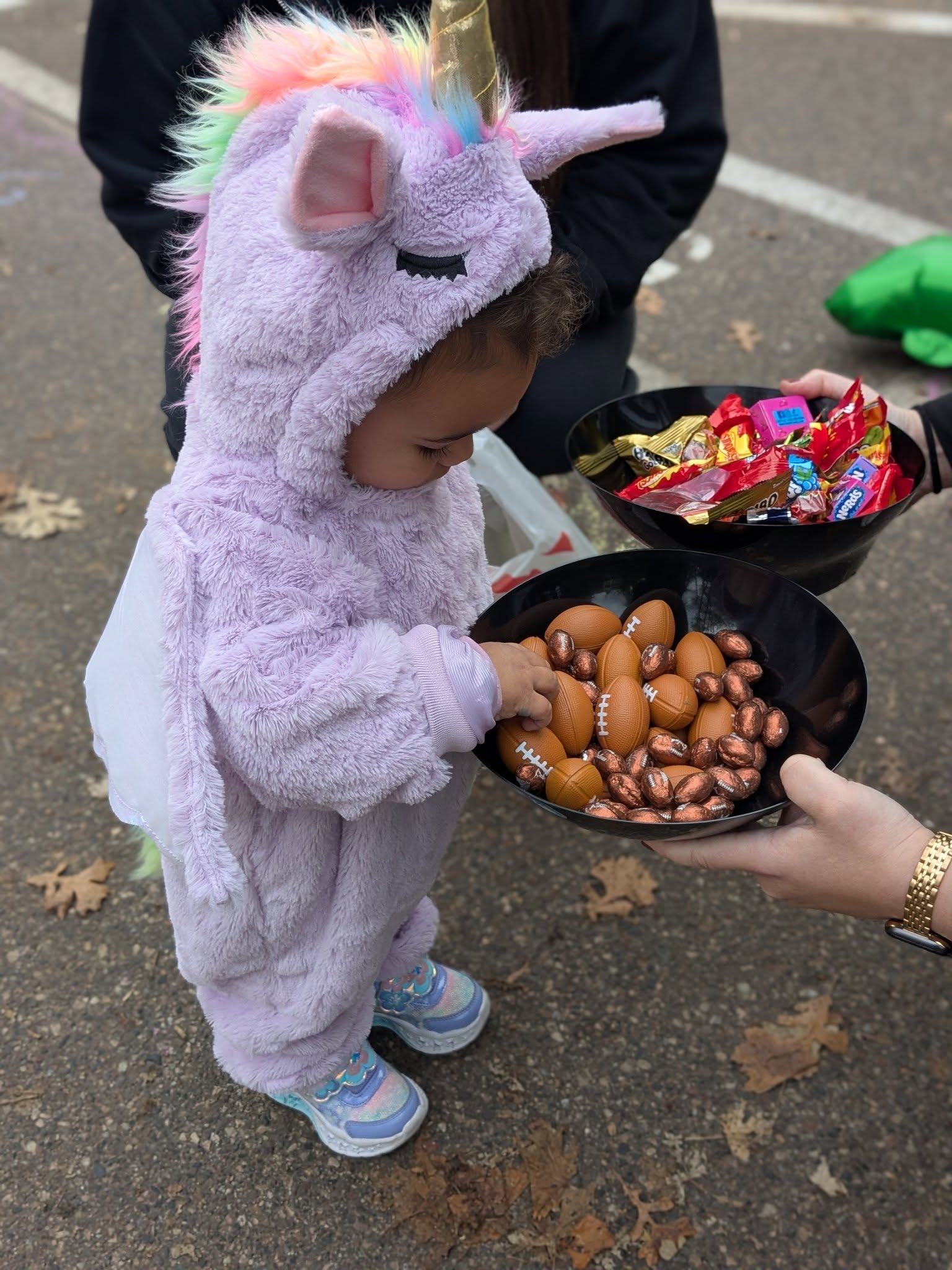 A toddler in a unicorn costume enjoying a Halloween trunk-or-treat event at Creative Kids Academy Maple Grove