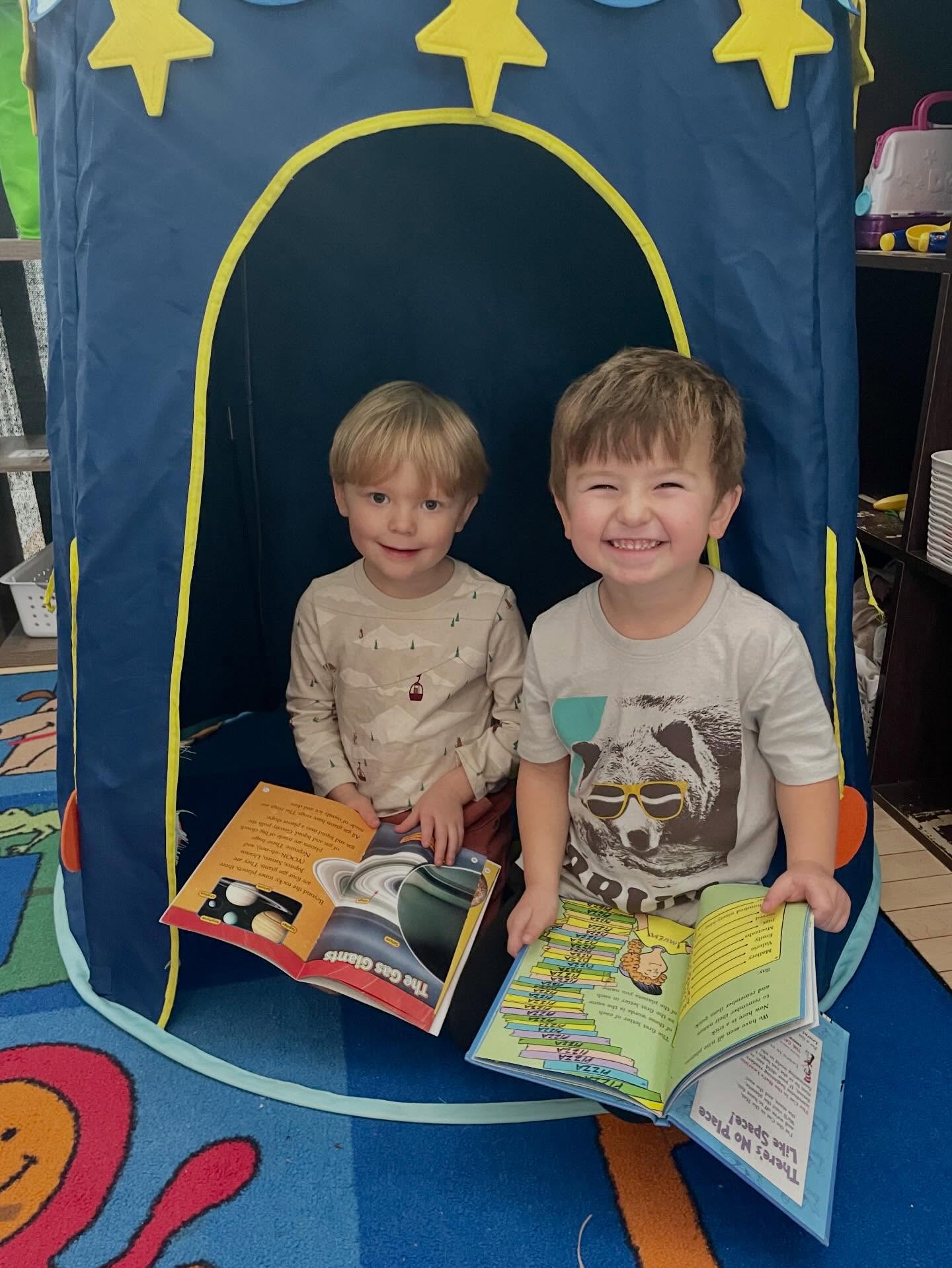 Two preschoolers reading books inside a rocket ship playhouse at Creative Kids Academy Orono