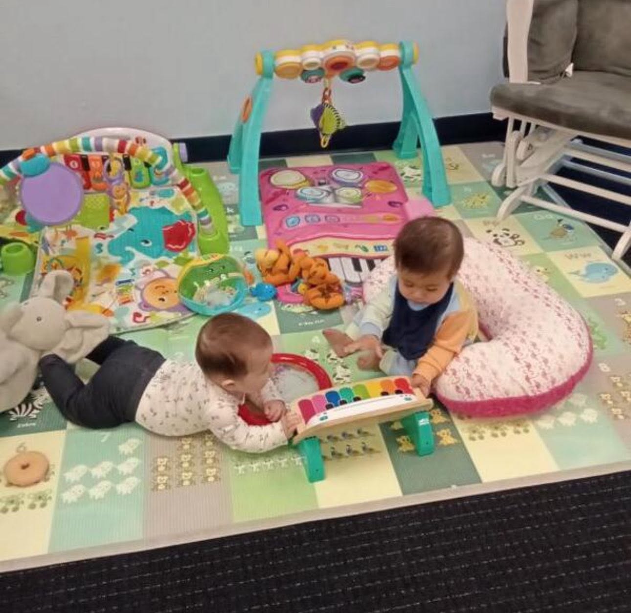 Two infants exploring toys together on an activity mat at Creative Kids Academy Centerville