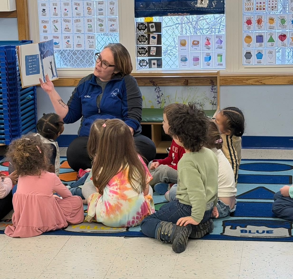 A CKA teacher reading a book to a circle of children