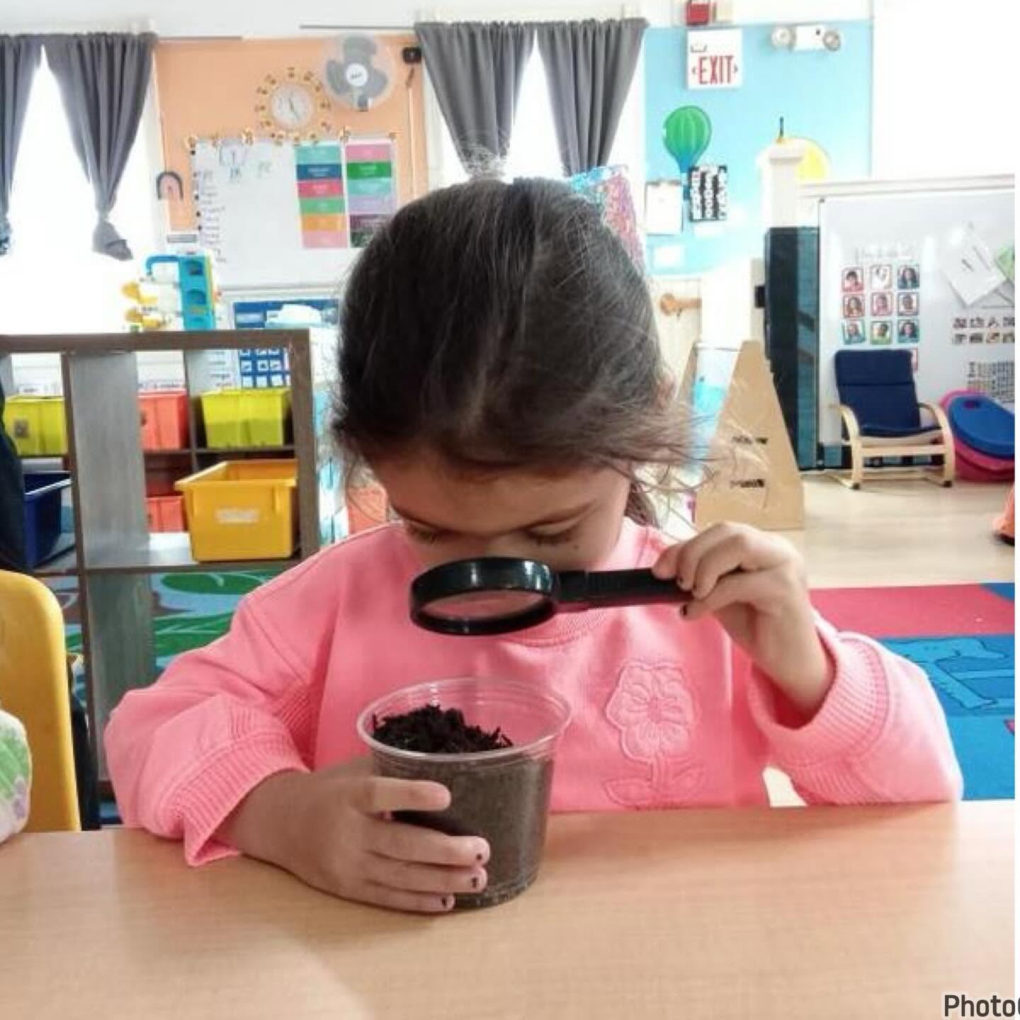 A preschooler exploring dirt with a magnifying glass during a science activity at Creative Kids Academy Orono