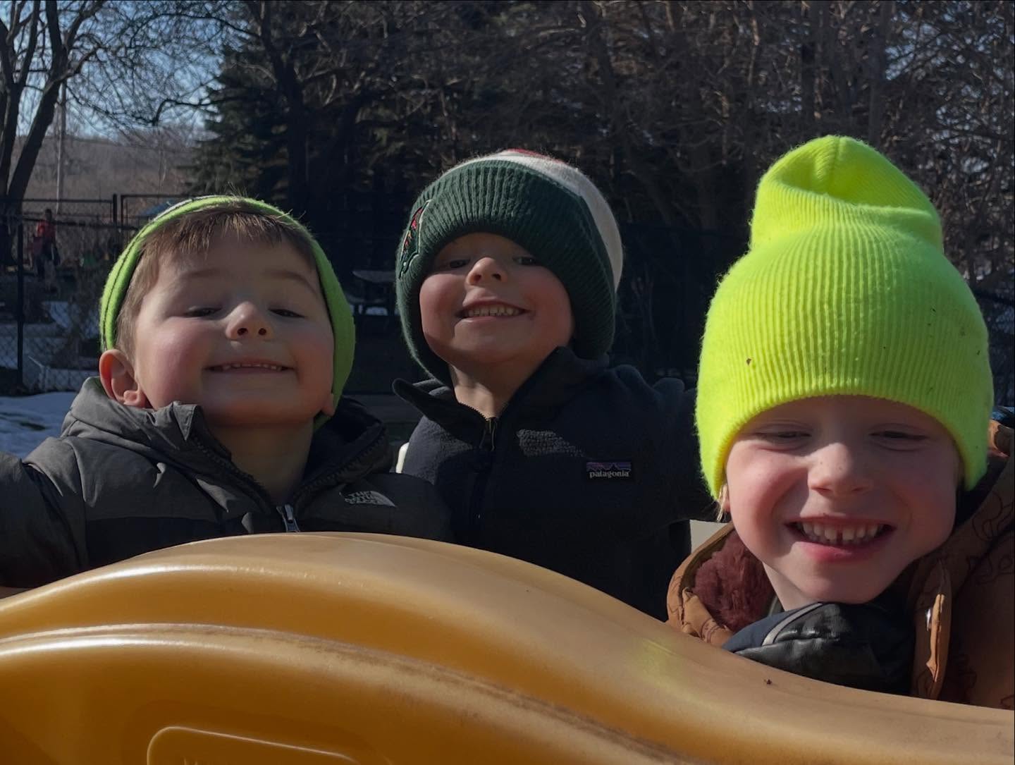 Three children bundled up in beanies enjoying outdoor play at Creative Kids Academy Orono