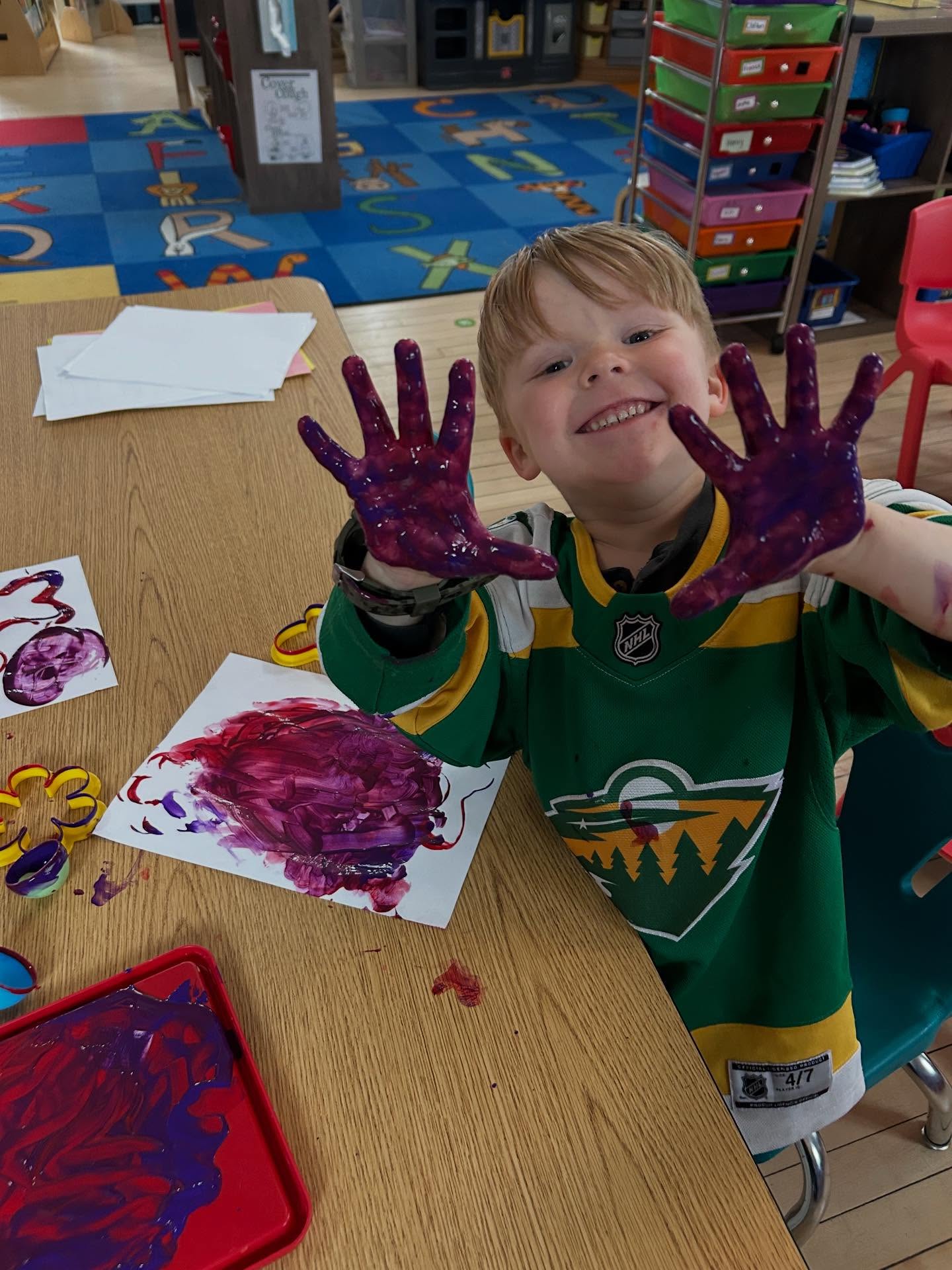 A preschooler showing off paint-covered hands during an art project at Creative Kids Academy Orono