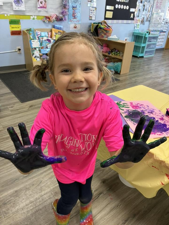 A preschooler proudly showing off her hands after a colorful painting activity at Creative Kids Academy Elk River