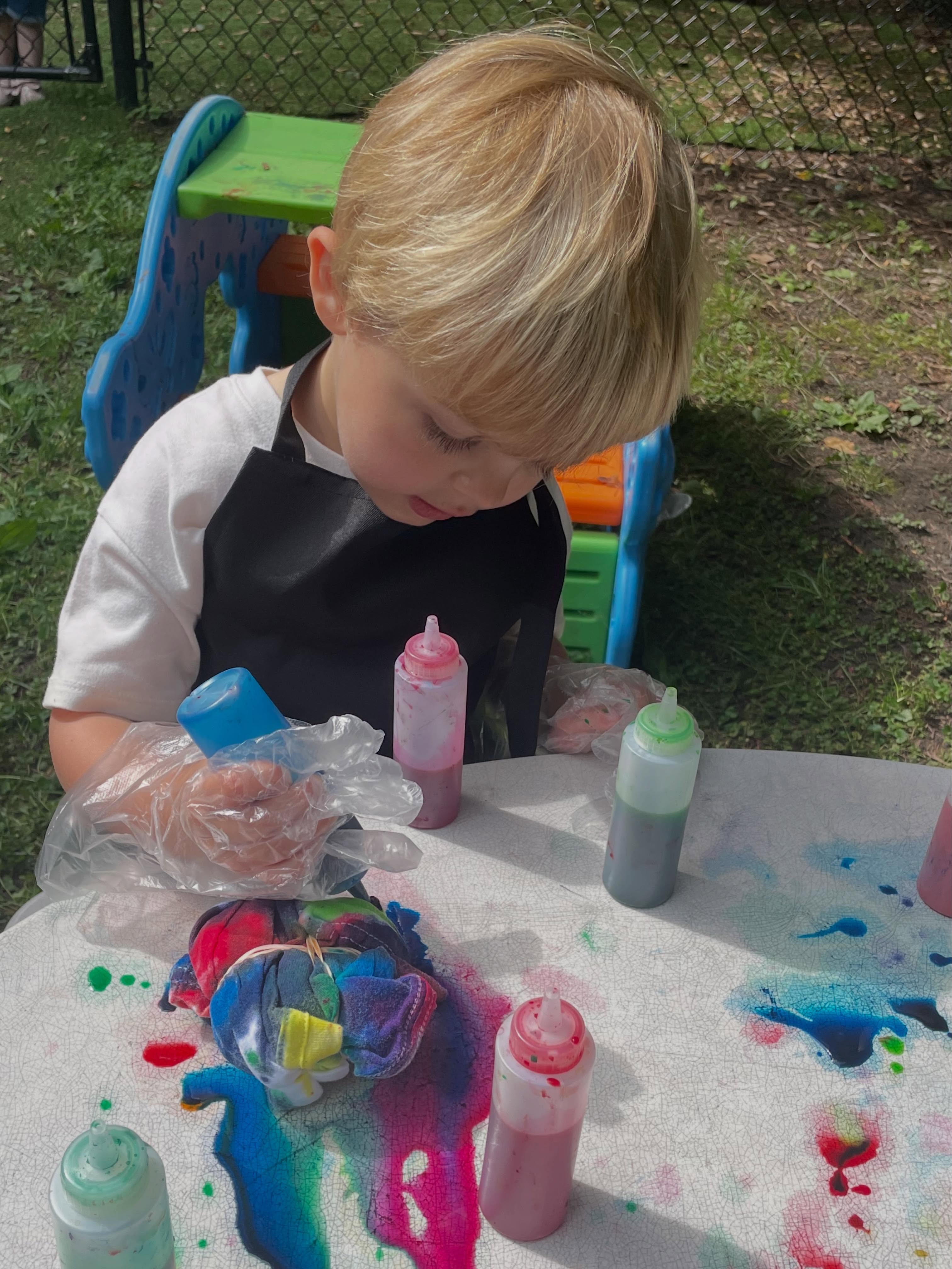 A preschooler tie-dyeing outdoors at Creative Kids Academy Orono