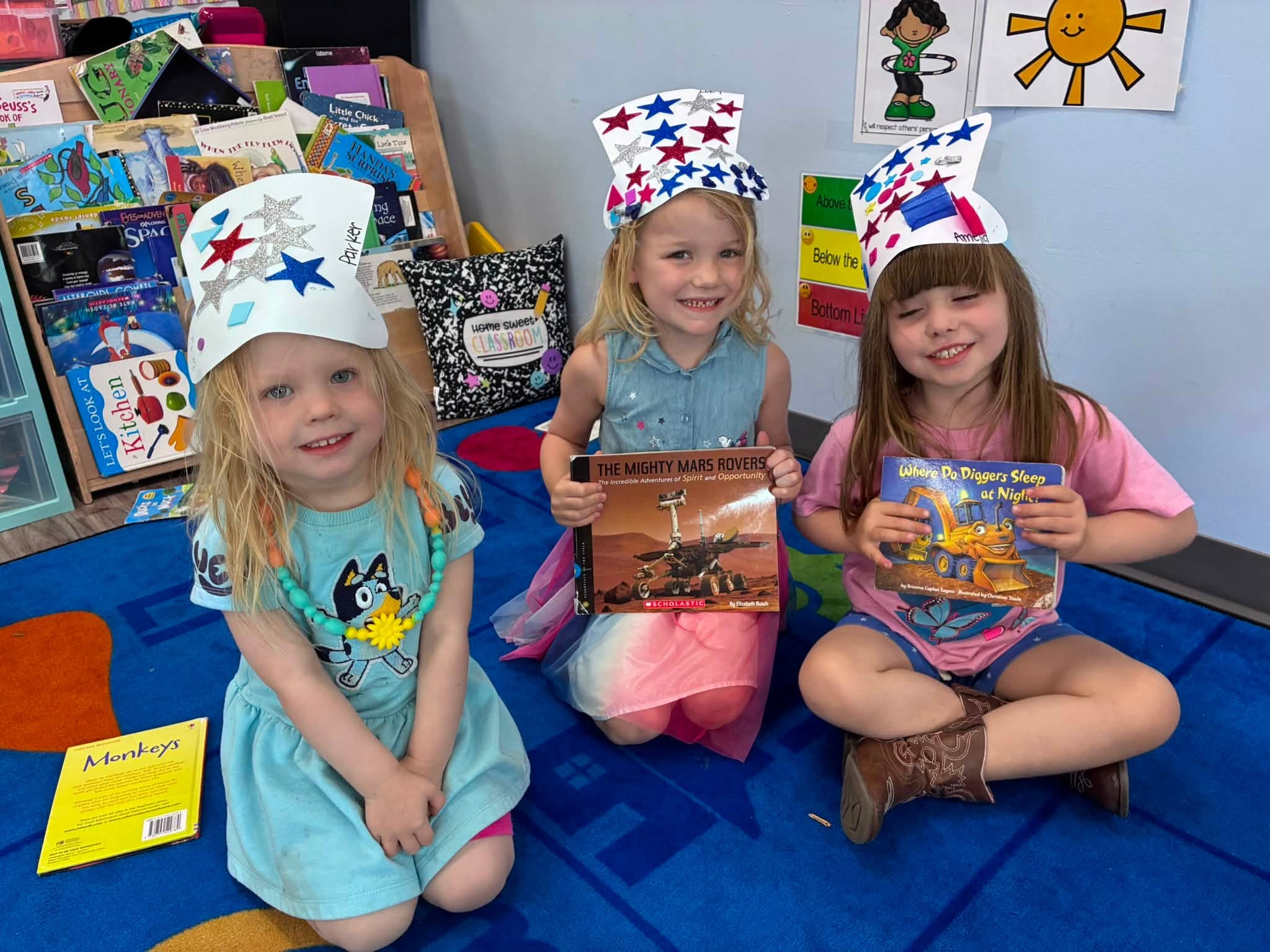 Preschoolers wearing handmade patriotic hats and holding books during a Fourth of July classroom activity at Creative Kids Academy Elk River