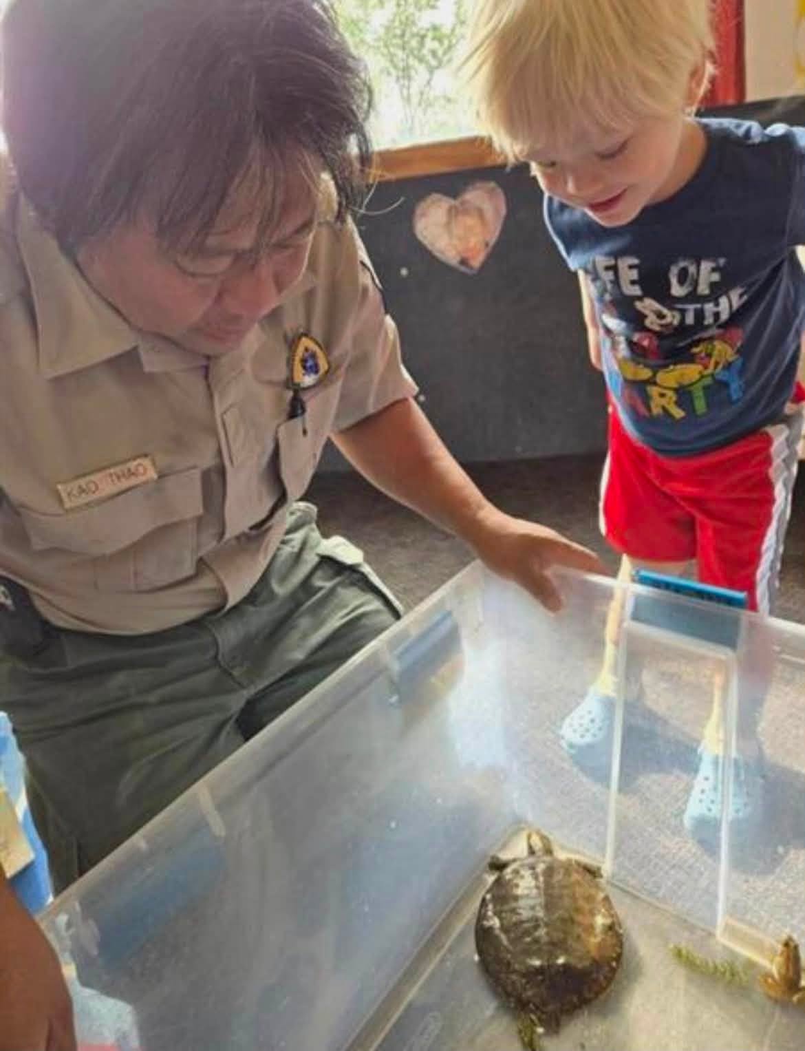 A school-age child examining a turtle with a visiting park ranger at Creative Kids Academy Minnetonka