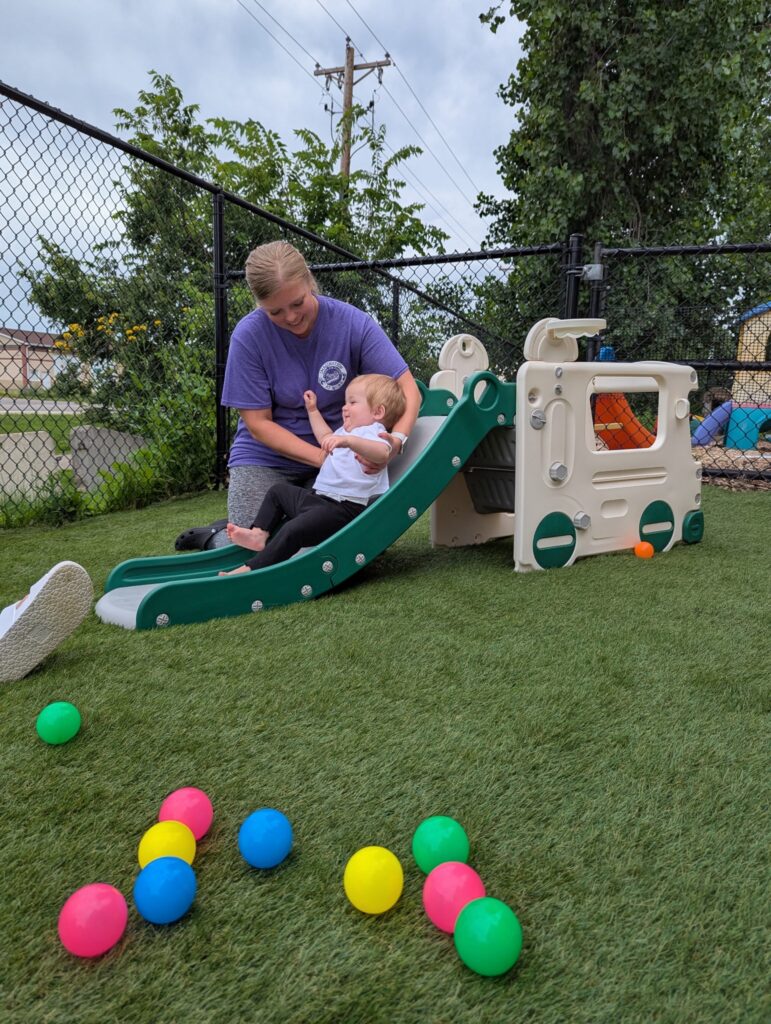 A Creative Kids Academy teacher going down a playground slide with a baby