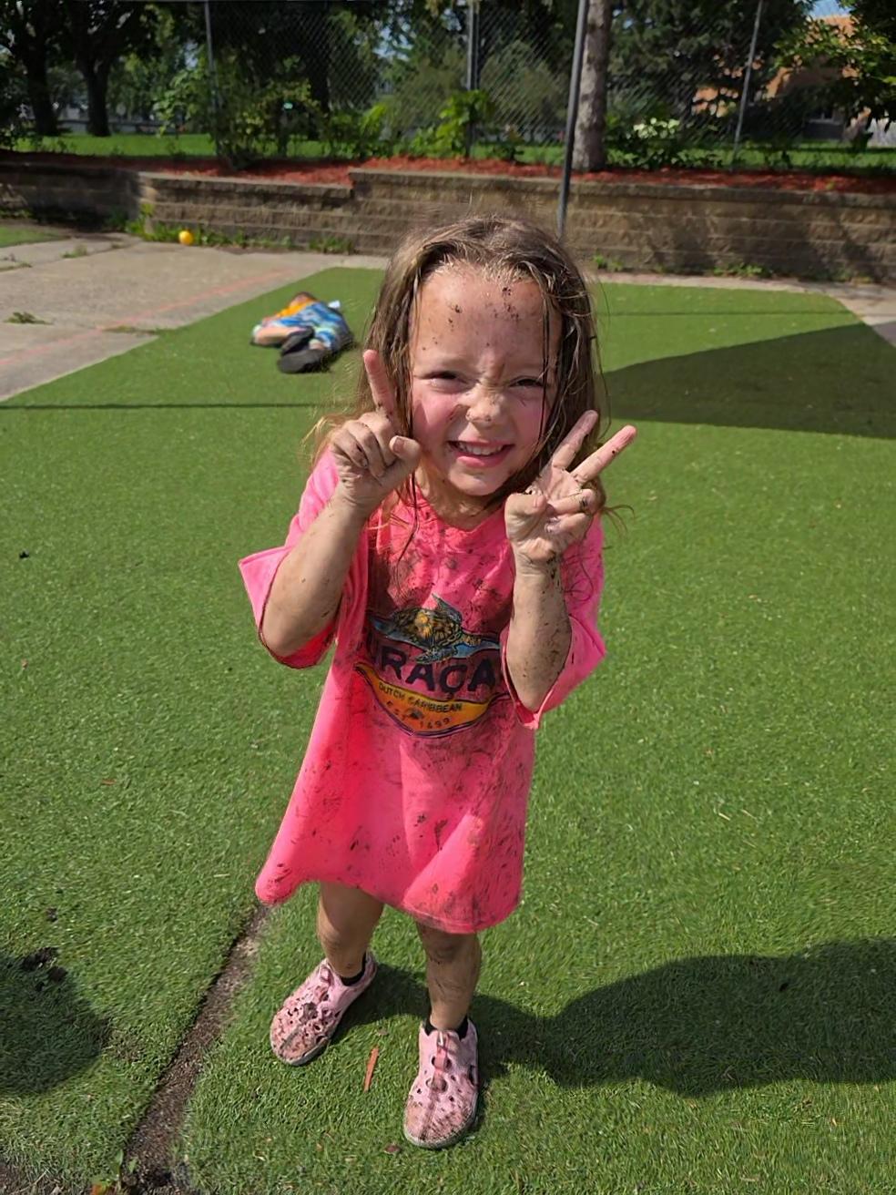 Preschooler flashing peace signs after messy outdoor play at Apple Valley