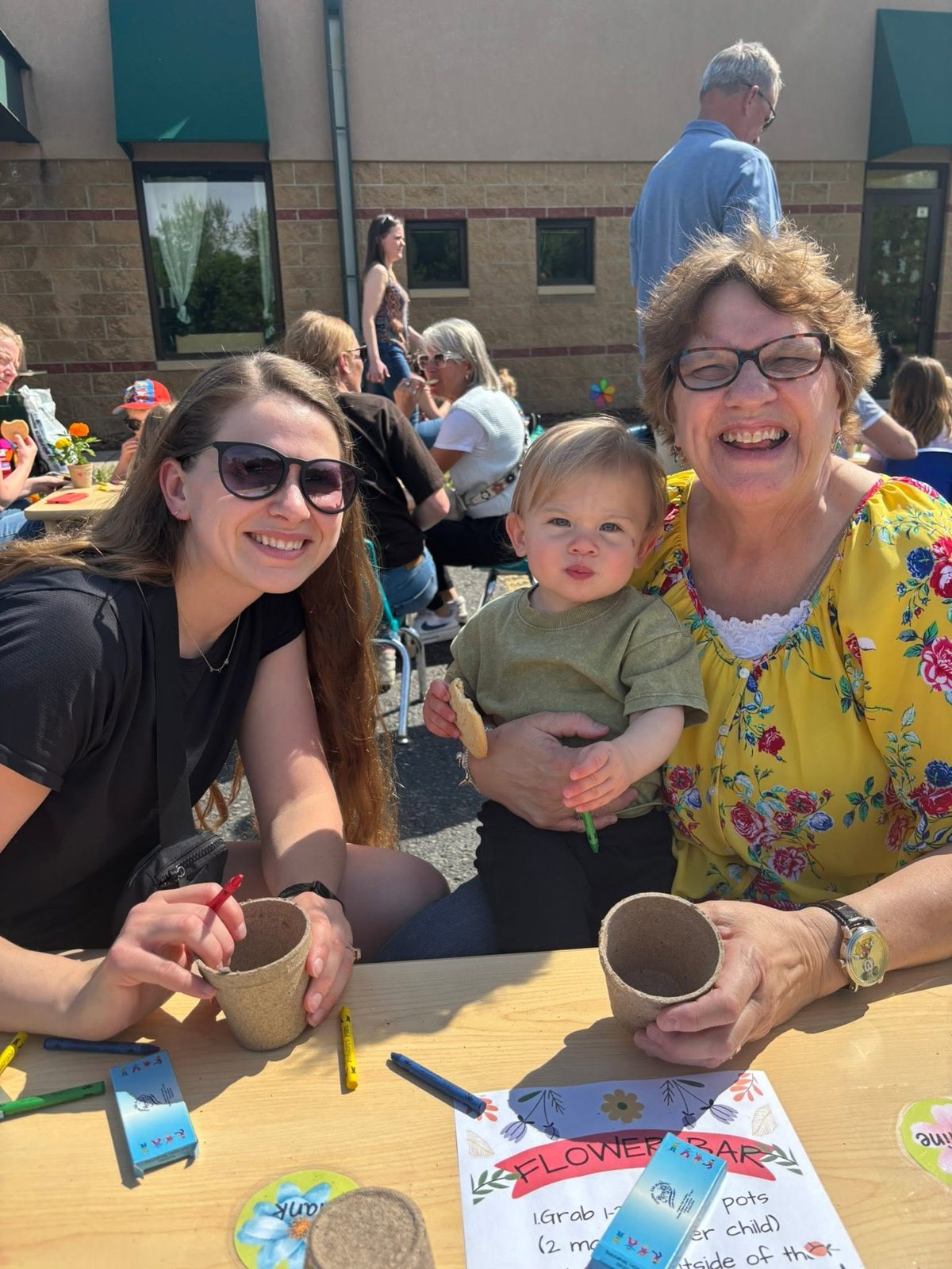 A mother, grandmother, and toddler smiling together at a Creative Kids Academy family event