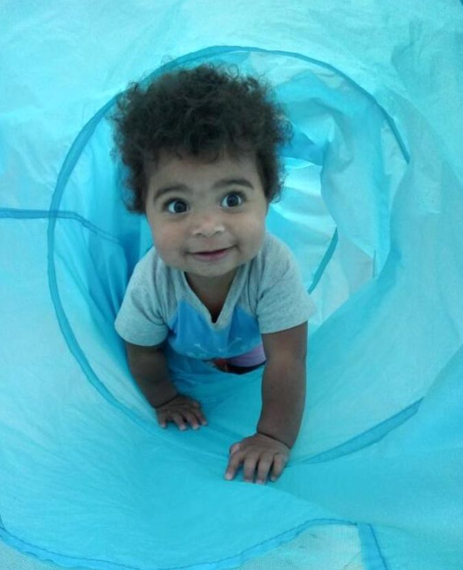 Smiling baby crawling through a play tunnel at Creative Kids Academy