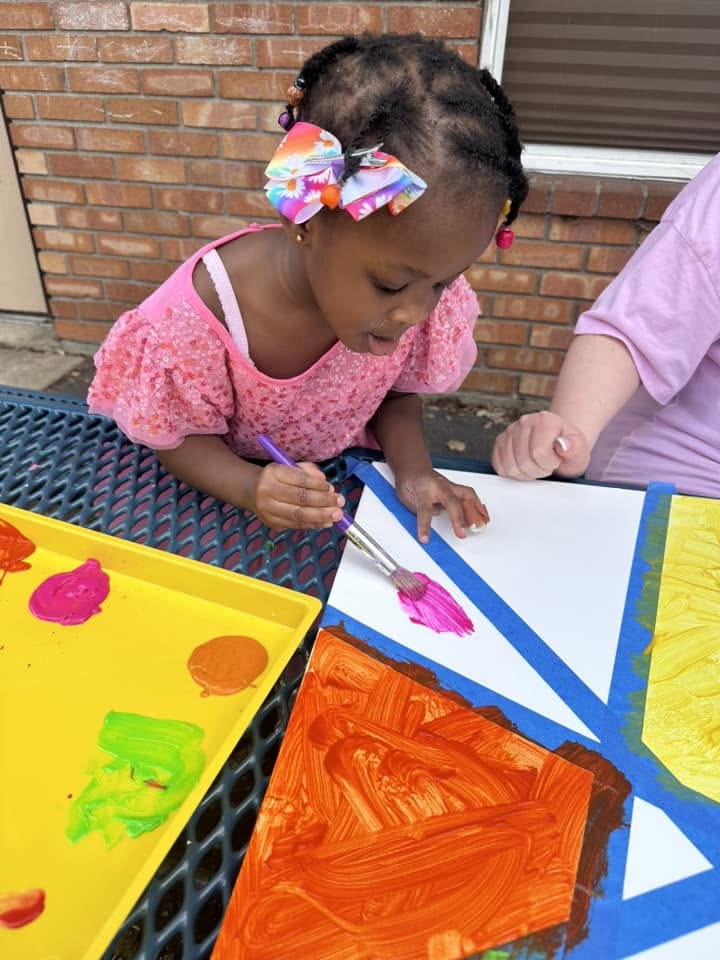 Toddler painting a bright canvas outdoors at Creative Kids Academy Coon Rapids
