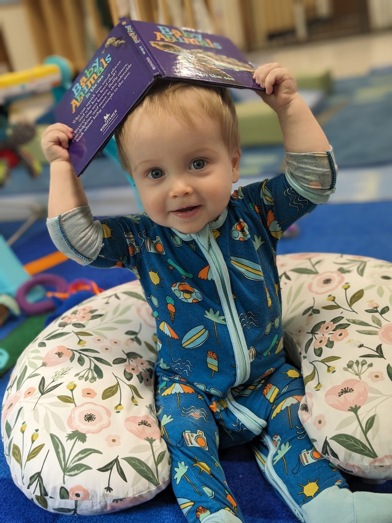 Baby holding a board book overhead in the infant room at Creative Kids Academy Maple Grove