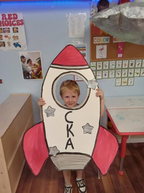 Preschooler peeking through a handmade CKA rocket ship at Creative Kids Academy Maplewood