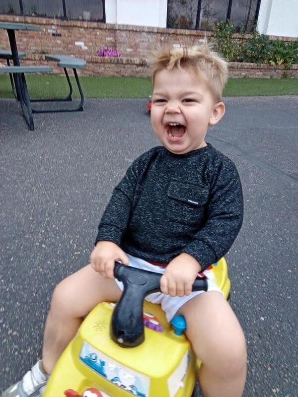 Laughing toddler riding a ride-on toy outside at Creative Kids Academy Minnetonka