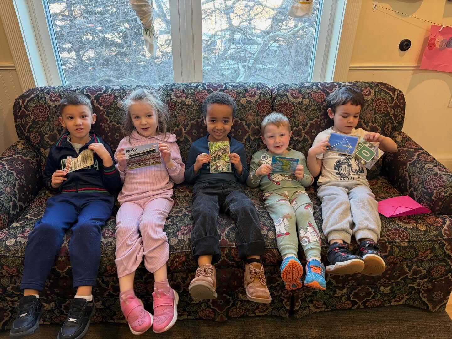 Preschool friends on the couch showing off postcards they received at Creative Kids Academy Orono