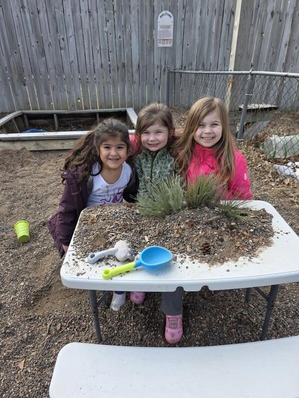 Three preschool friends digging together at the outdoor sensory table at Creative Kids Academy Zimmerman