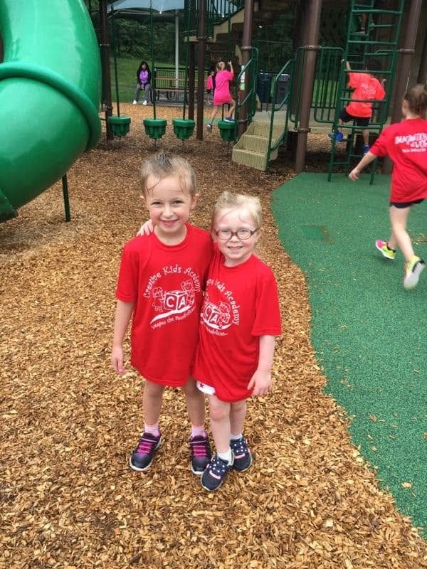 Two friends in Creative Kids Academy t-shirts on the playground at Creative Kids Academy Mounds View