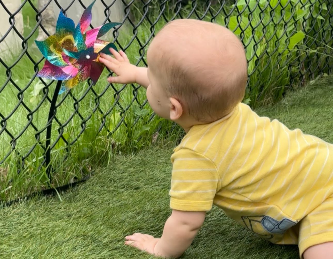 Baby reaching for a colorful pinwheel on the playground at Creative Kids Academy