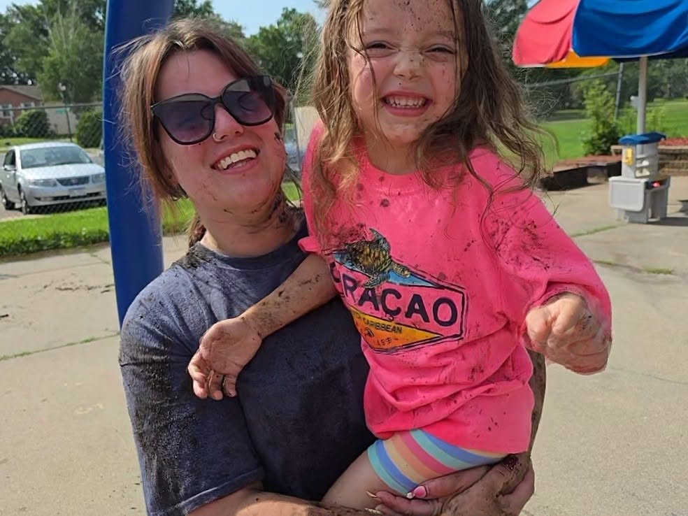 A teacher and a mud-covered preschooler laughing together during summer outdoor play at Creative Kids Academy